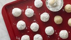 there are many snowball cookies on the red tray with a small bowl of powdered sugar