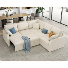 a white sectional sofa with blue pillows on it in a large living room area next to a dining table