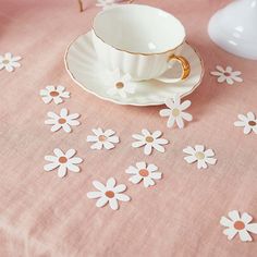 a cup and saucer sitting on top of a table covered in white daisies