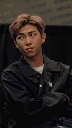 a young man with his arms crossed sitting in front of a black backdrop and looking at the camera