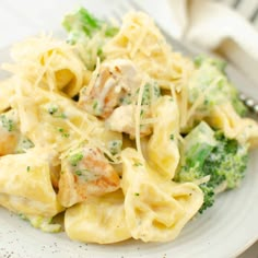 a white plate topped with pasta and broccoli covered in cheese sauce next to a fork