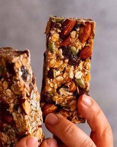 someone holding up two granola bars with nuts and raisins