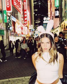 a woman in bunny ears stands on the street at night with people walking around her