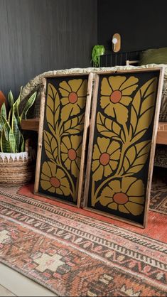 two wooden panels with flowers on them sitting on a rug next to a potted plant