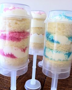 three desserts in plastic containers sitting on a wooden table with white frosting and pink, blue, and green sprinkles