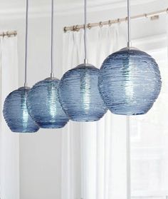 three blue glass globes hanging from a ceiling in a room with large windows and potted plant