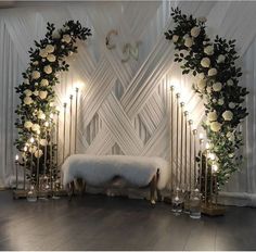 a room with white flowers and candles on the floor next to a bench in front of a wall