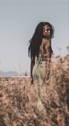 a woman standing in tall grass with her back to the camera and looking off into the distance