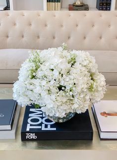 a vase with white flowers on top of two books sitting on a table in front of a couch