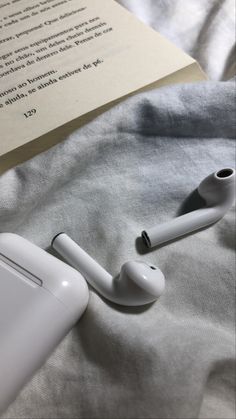 an apple airpods sitting on top of a bed next to a book and pen