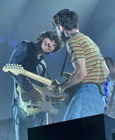 two young men are playing guitars on stage