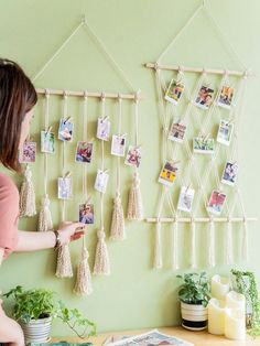 a woman hanging pictures on a wall with macrame tassels attached to it