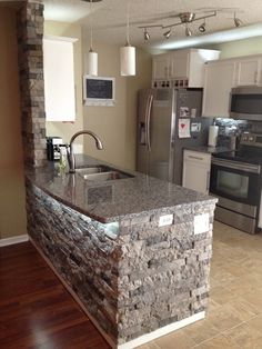 a kitchen with an island made out of stone and stainless steel appliances in the background