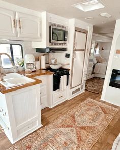 a kitchen with white cabinets and wood flooring next to a bed in a room that has an area rug on the floor