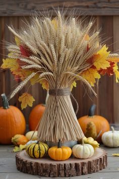 an arrangement of pumpkins, gourds and wheat stalks on a wooden table