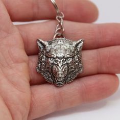 a hand holding a metal keychain with a wolf head on it's face