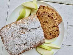 two slices of apple cake on a white plate with sliced apples and powdered sugar