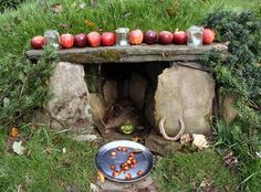 an outdoor area with apples and candles on the table, near a stone bench that has been built into the ground