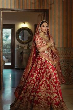 a woman in a red and gold bridal gown posing for the camera with her hands on her hips