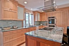 a kitchen with wooden cabinets and marble counter tops, along with an island in the middle