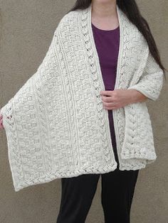 a woman wearing a white knitted cardigan standing in front of a gray wall