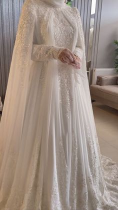 a woman in a white wedding gown with a veil on her head, standing next to a couch