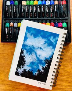 an artist's watercolor set with a box of paint and a notebook on the table