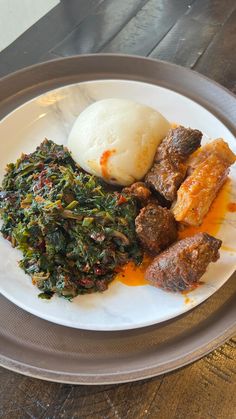 a white plate topped with meat, greens and mashed potatoes on top of a wooden table