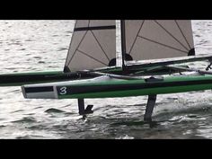 a green and black boat with two sails in the water on a lake or body of water