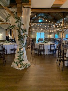 an indoor wedding venue with white linens and greenery on the ceiling, decorated with fairy lights