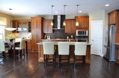 a large kitchen with wooden floors and white chairs around the island, along with stainless steel appliances