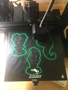 a large black and green printer sitting on top of a wooden table next to a camera