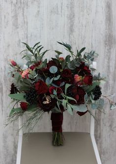 a bouquet of red flowers and greenery sits on a table in front of a white wall