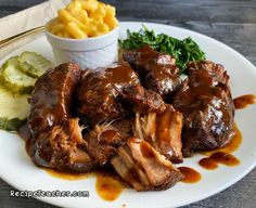 a white plate topped with meat covered in gravy next to potatoes and greens