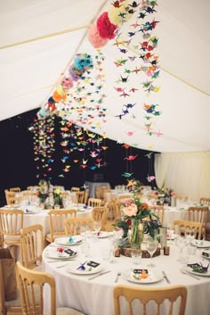 the tables are set with white linens and colorful paper cranes hanging from the ceiling