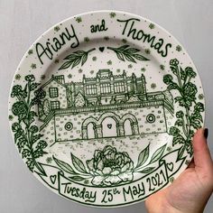 a hand holding a plate with a drawing of a house and flowers on it that says albany and thomas