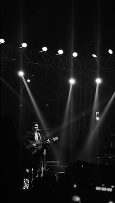 black and white photo of man playing guitar on stage with lights in the dark behind him