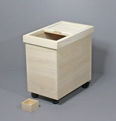 a small wooden trash can sitting next to a block of wood on top of a gray floor