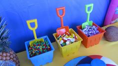 a table topped with plastic containers filled with candies and pineapples next to a blue wall