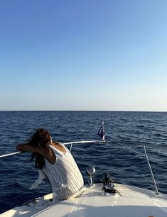 a woman sitting on the back of a boat looking out over the ocean at a sailboat