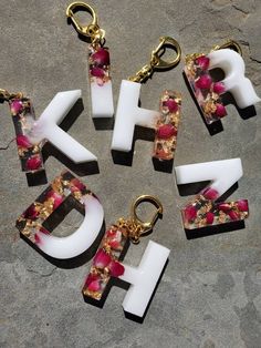 the letters are made out of plastic and have flowers on them, as well as gold - plated key chains