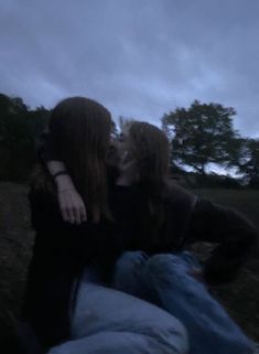 two people sitting on the ground kissing each other with trees in the back ground behind them