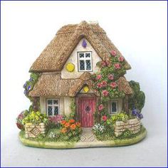 a figurine of a house with flowers and plants on the outside, in front of a white background