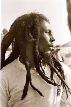 a man with dreadlocks standing in front of a sign that says, one love, one heart let's get together and feel alright