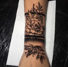 a black and white flower tattoo on the wrist, with an arrow in the middle