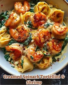 pasta with shrimp and spinach in a white bowl on top of a black table