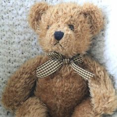 a brown teddy bear sitting on top of a white carpet with a checkered bow around it's neck