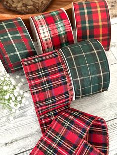 four plaid ribbon rolls are lined up on a white wooden surface with flowers in the background