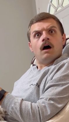 a man sitting in a chair holding a remote control with his mouth wide open and looking surprised