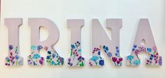 the letters are made up of flowers and have been painted pink, blue, green, purple, and white